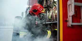 ein Feuerwehrmann kniet vor einem Feuerwehrauto im Nebel (Rauch)