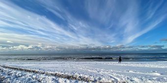 Das Motiv zeigt den Strand mit Schnee und blauem Himmel.