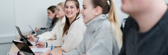 Das Foto zeigt mehrere junge Menschen, die an einem Tisch in einem Unterrichtsraum sitzen und an etwas arbeiten.
